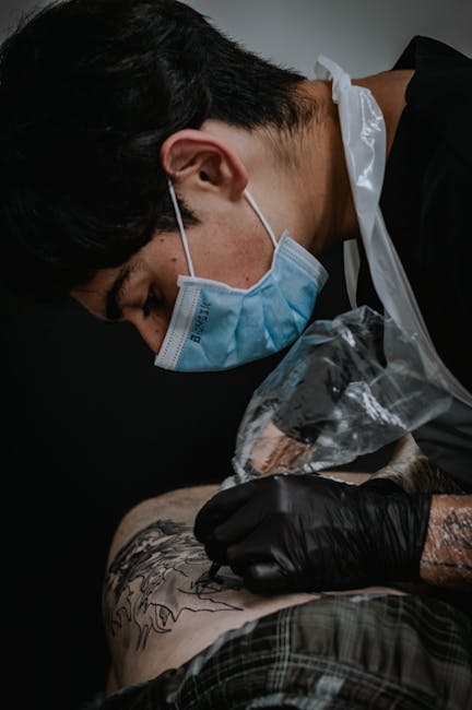 Artista del tatuaje concentrado trabajando con máscara y guantes en estudio profesional